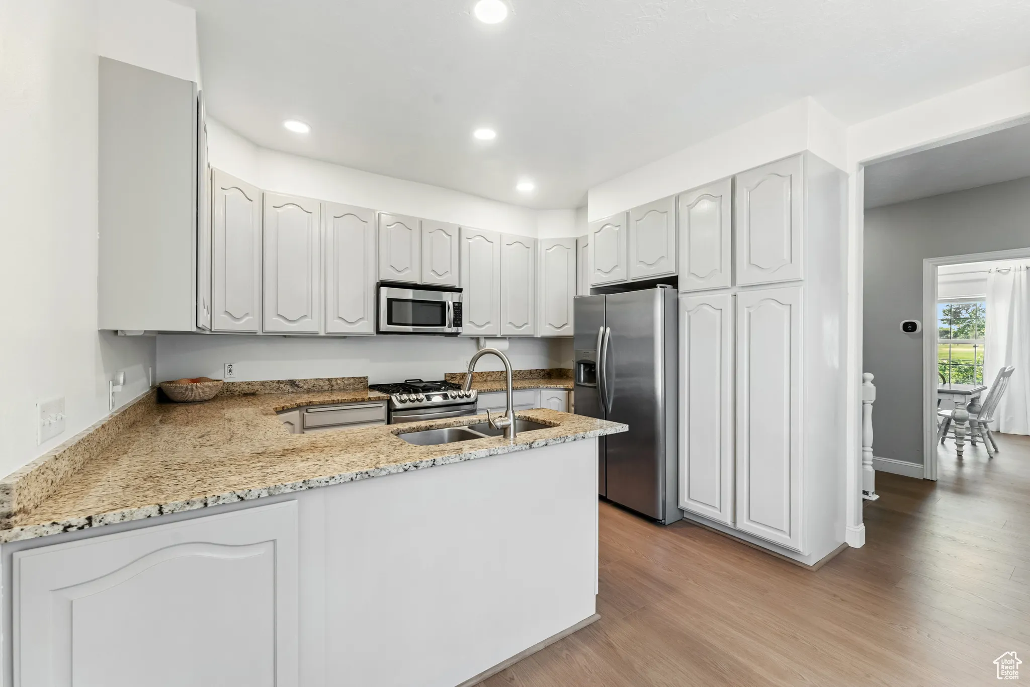 Kitchen with light wood-type flooring, appliances with stainless steel finishes, a peninsula, light stone countertops, and recessed lighting