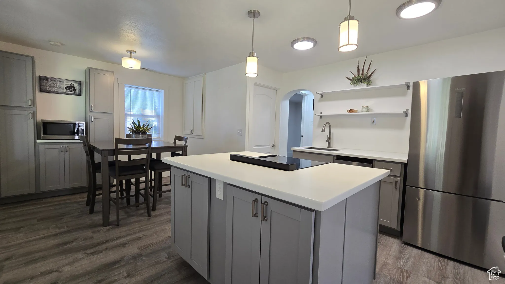 Kitchen featuring gray cabinetry, appliances with stainless steel finishes, arched walkways, and dark wood-style flooring