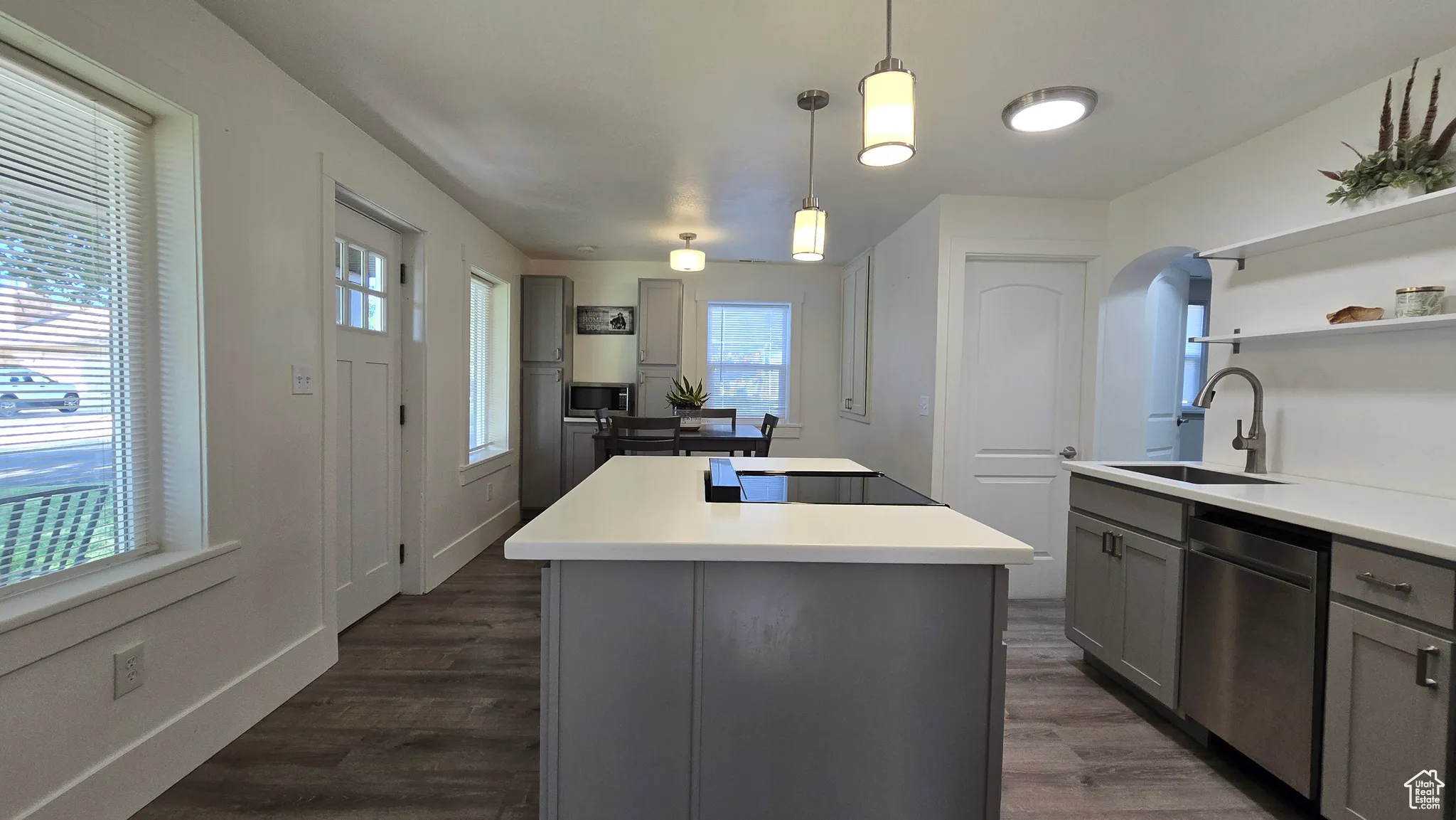 Kitchen with gray cabinets, a center island, dark wood-style floors, stainless steel dishwasher, and open shelves