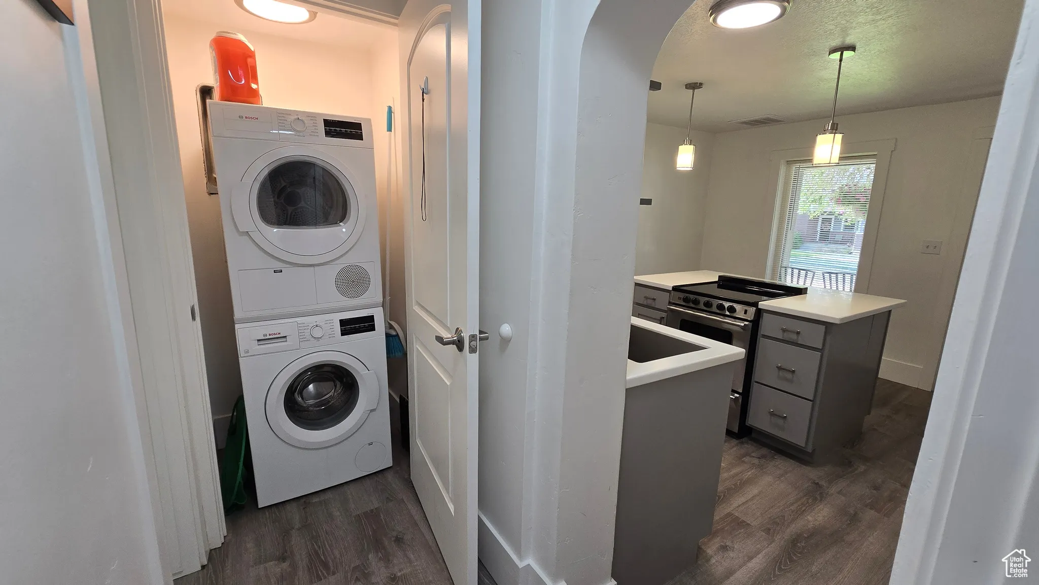Laundry area featuring stacked washer / dryer, arched walkways, dark wood-style floors, and a textured ceiling