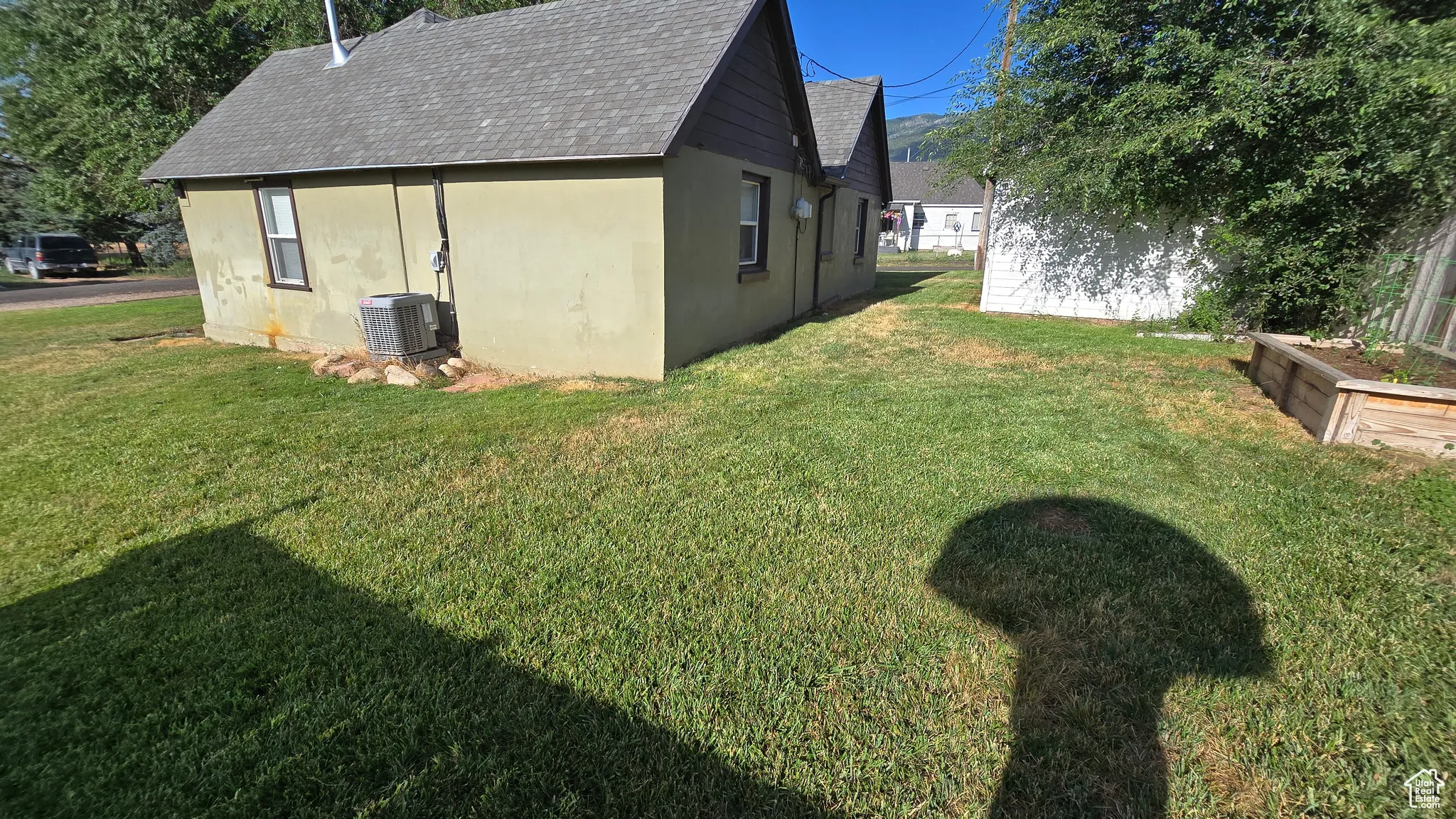 View of side of home featuring stucco siding, a lawn, and roof with shingles