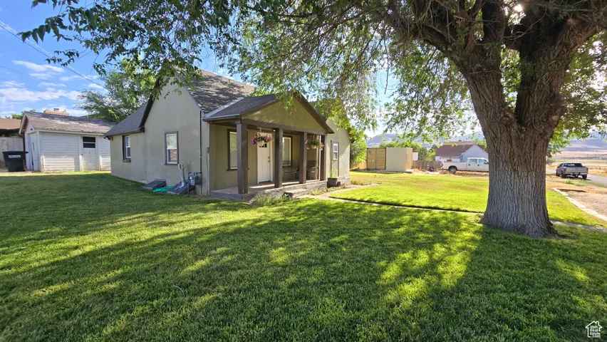 Back of house featuring a shingled roof, a yard, and stucco siding
