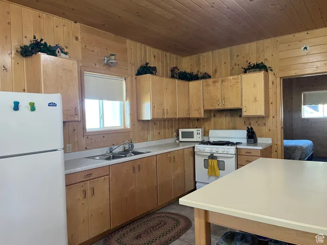 Kitchen featuring white appliances, light countertops, wooden ceiling, and wooden walls