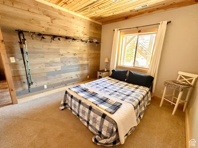 Carpeted bedroom featuring wooden ceiling and wooden walls