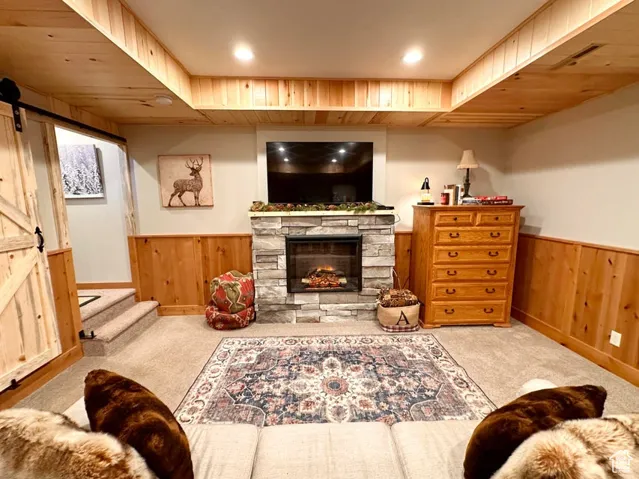 Carpeted living room with wood walls, a wainscoted wall, a barn door, a fireplace, and recessed lighting