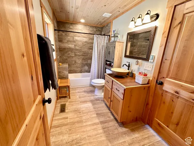 Bathroom featuring vanity, shower / bath combo with shower curtain, wooden ceiling, and wood finished floors