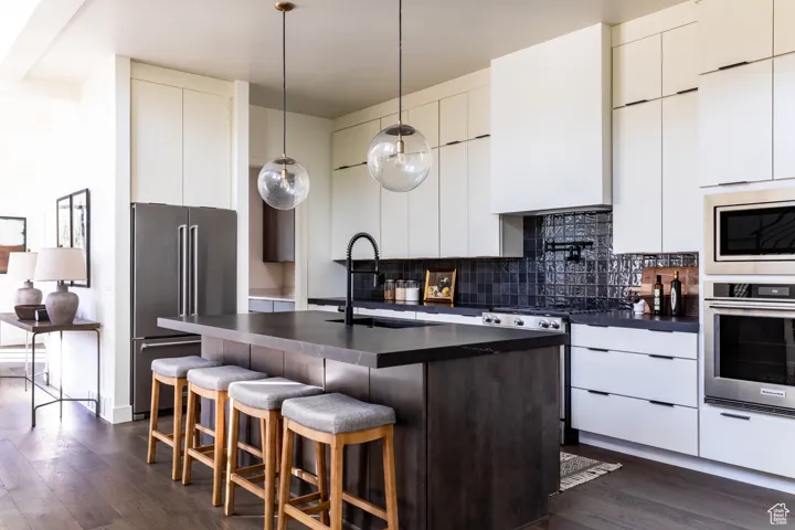 Kitchen with modern cabinets, dark countertops, dark wood-type flooring, and backsplash