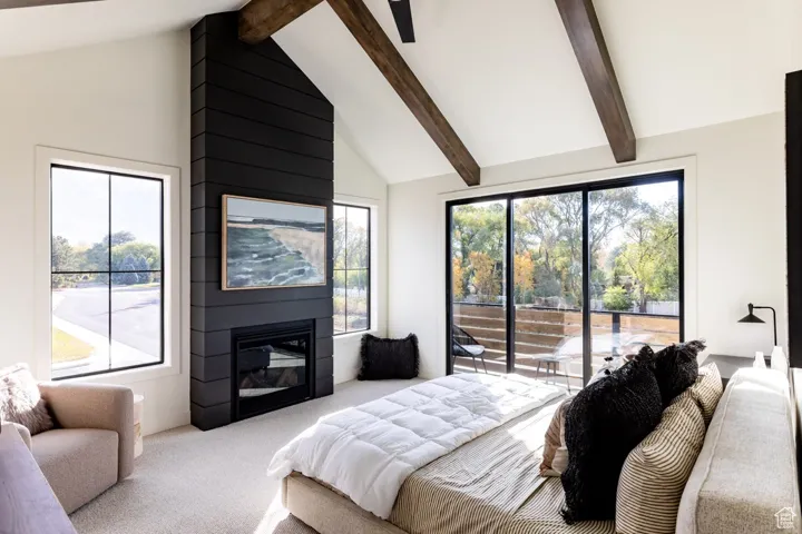 Carpeted bedroom featuring beamed ceiling, access to outside, a fireplace, and high vaulted ceiling