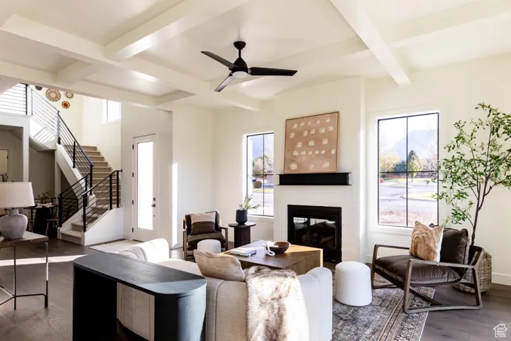 Living room featuring wood finished floors, beamed ceiling, a brick fireplace, coffered ceiling, and healthy amount of natural light