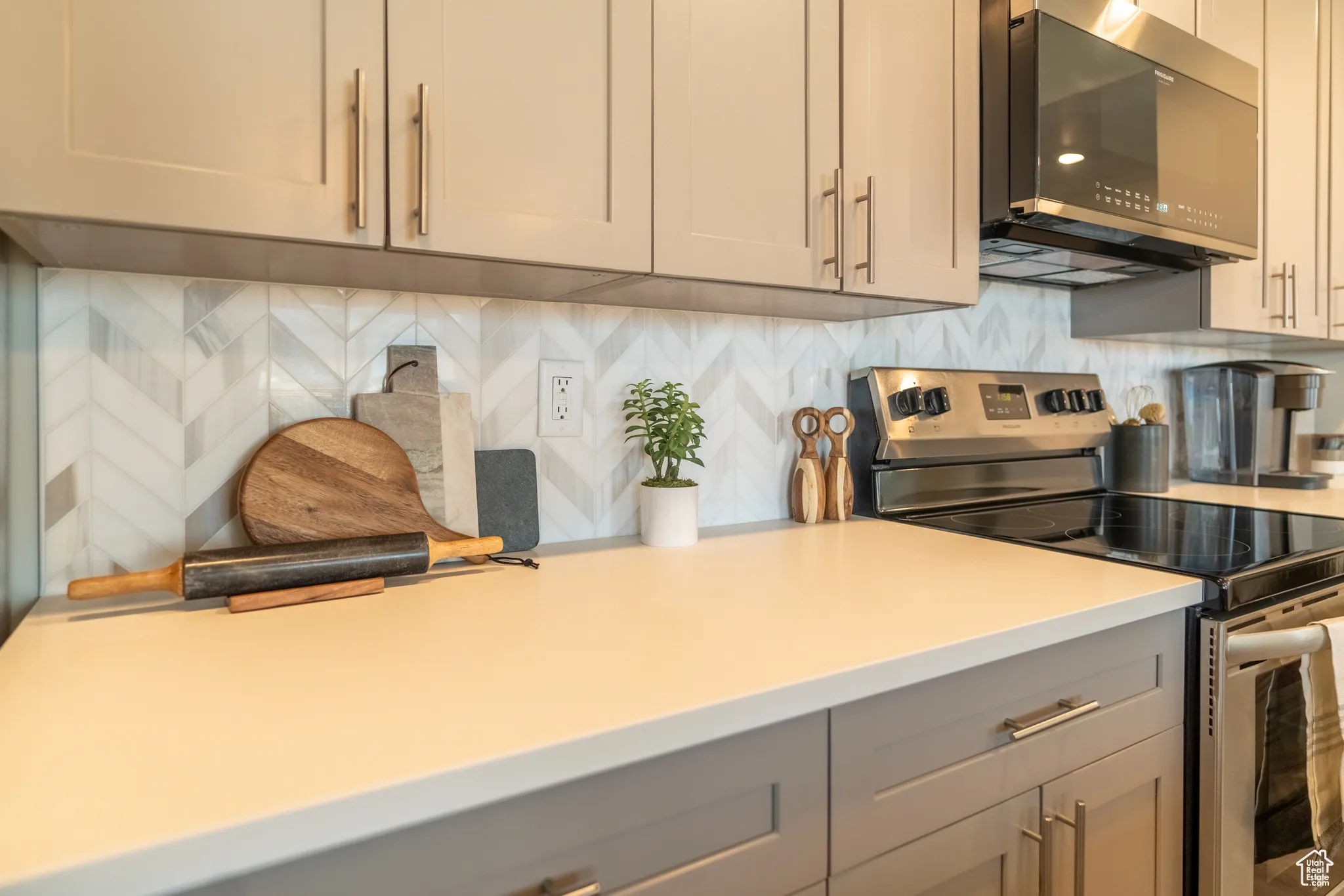 Kitchen with stainless steel electric range oven, gray cabinets, light countertops, and backsplash