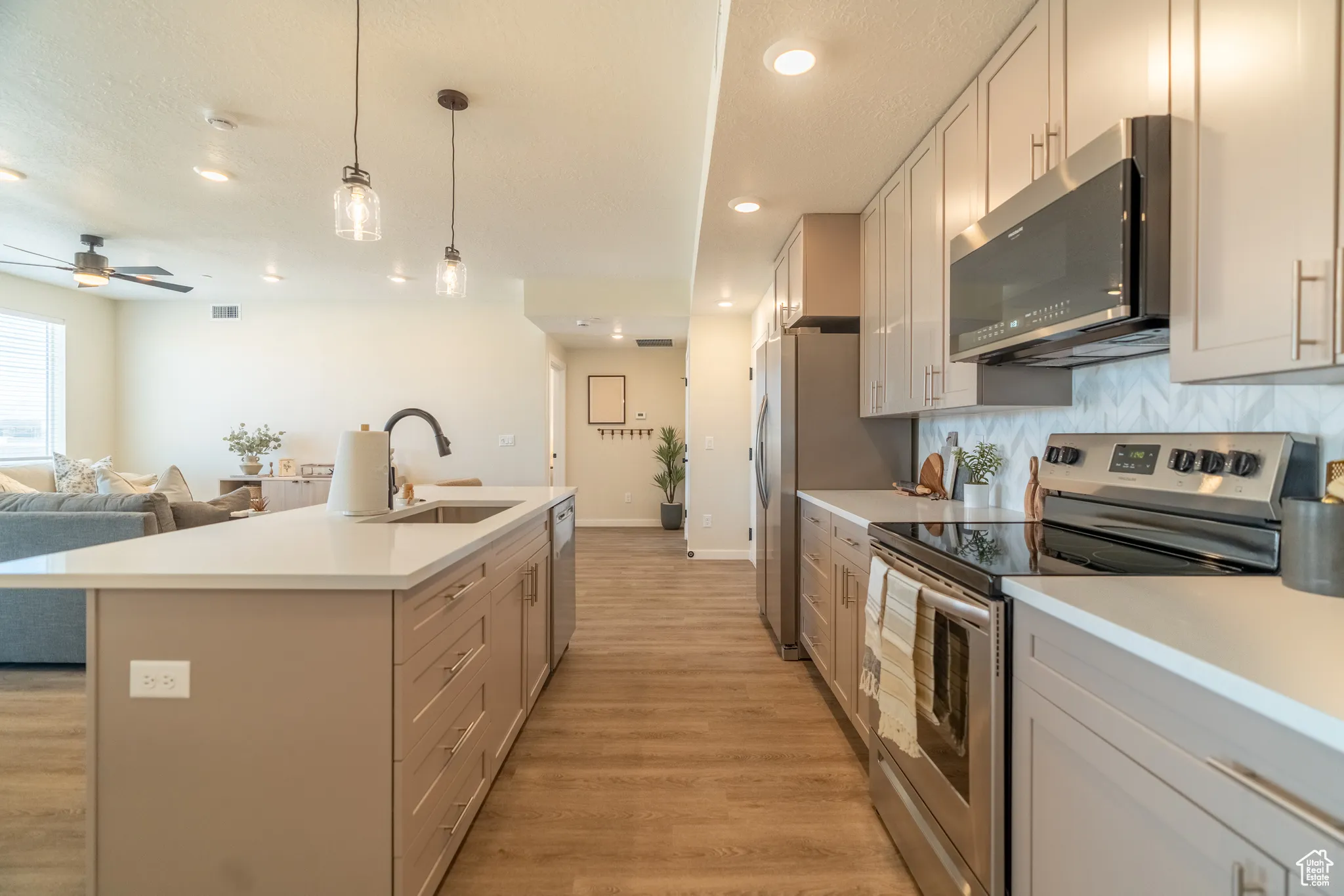 Kitchen featuring stainless steel appliances, open floor plan, light wood-style flooring, light countertops, and ceiling fan