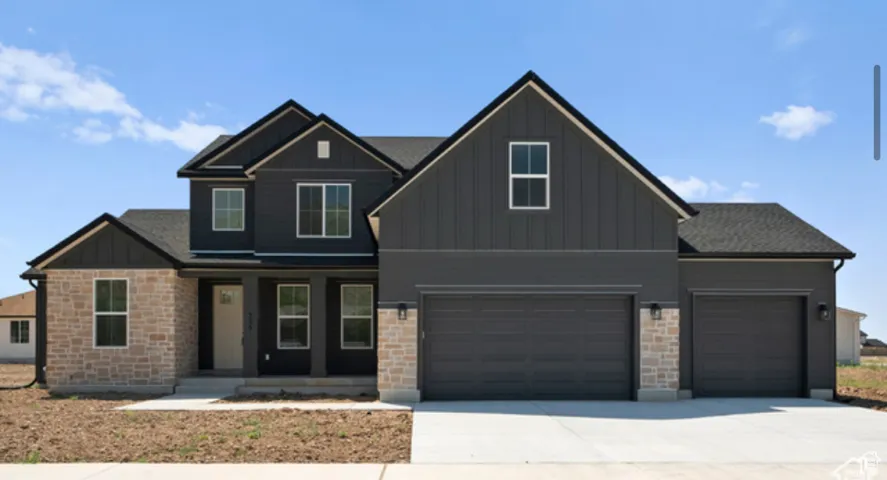 View of front of property with board and batten siding, a porch, stone siding, driveway, and an attached garage
