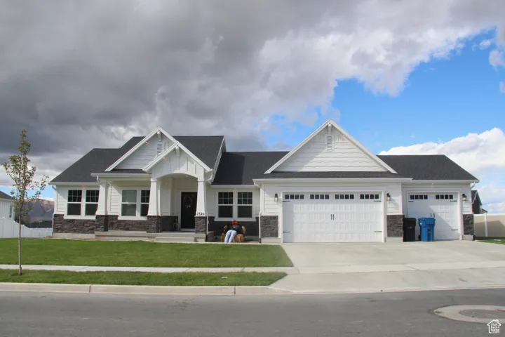 Craftsman-style house with a garage, concrete driveway, a front lawn, and stone siding