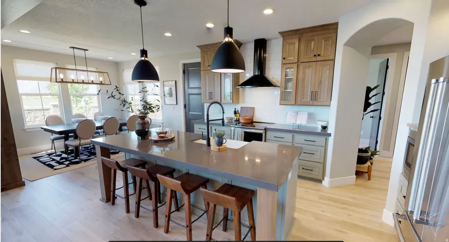 Kitchen featuring a center island with sink, decorative backsplash, wall chimney range hood, stainless steel appliances, and light wood-type flooring
