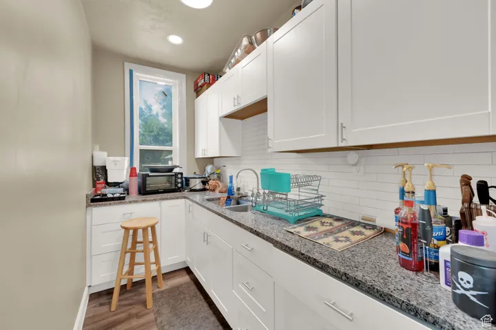 Kitchen with white cabinetry, decorative backsplash, light wood-style floors, light stone counters, and recessed lighting