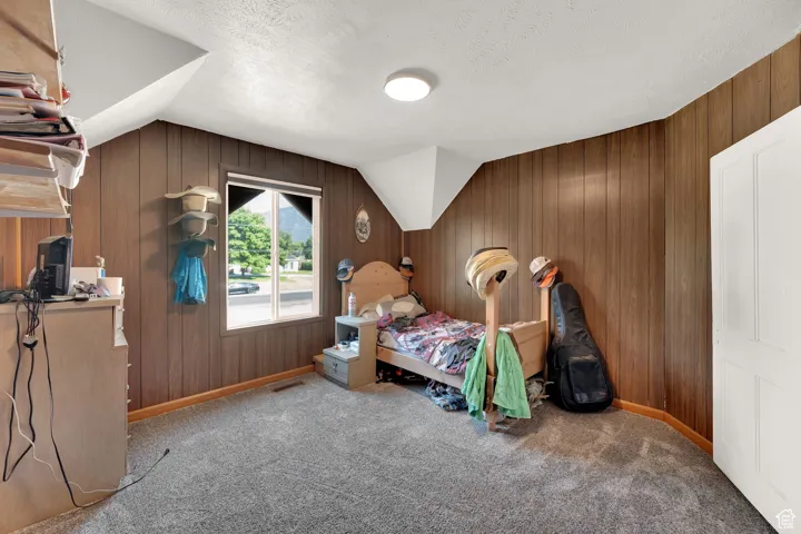 Bedroom featuring wood walls, carpet flooring, lofted ceiling, and a textured ceiling