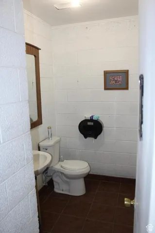 Half bathroom featuring dark tile patterned floors, crown molding, and concrete block wall