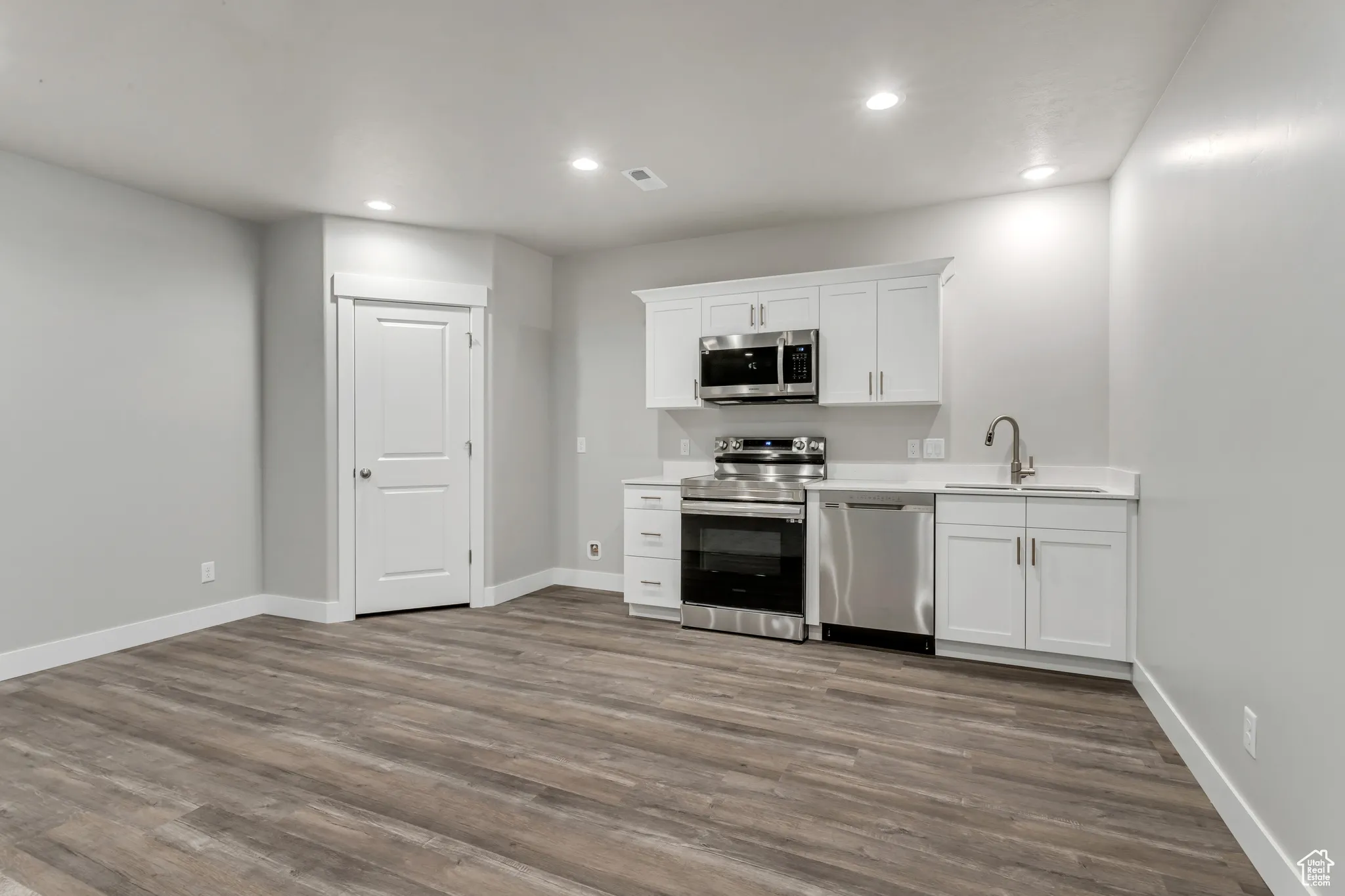 Kitchen with appliances with stainless steel finishes, recessed lighting, dark wood-style flooring, light countertops, and white cabinets