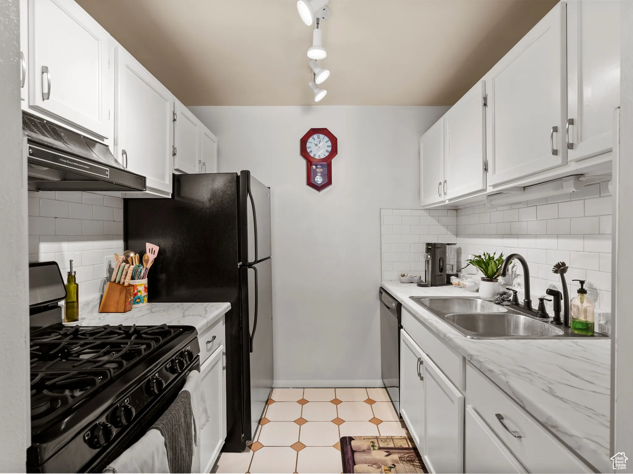 Kitchen with backsplash, black gas range, white cabinetry, under cabinet range hood, and light floors