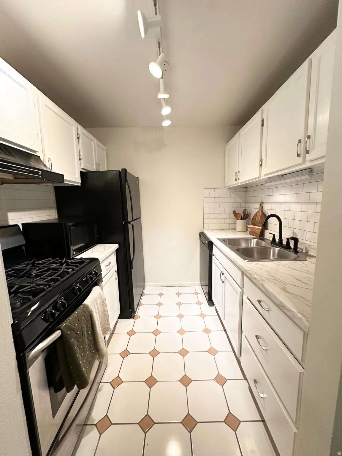 Kitchen featuring black appliances, tasteful backsplash, white cabinetry, and light countertops