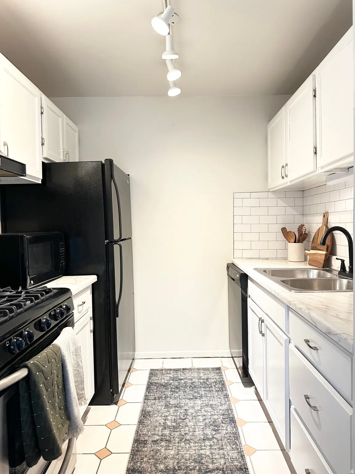 Kitchen with white cabinetry, black appliances, light countertops, decorative backsplash, and track lighting