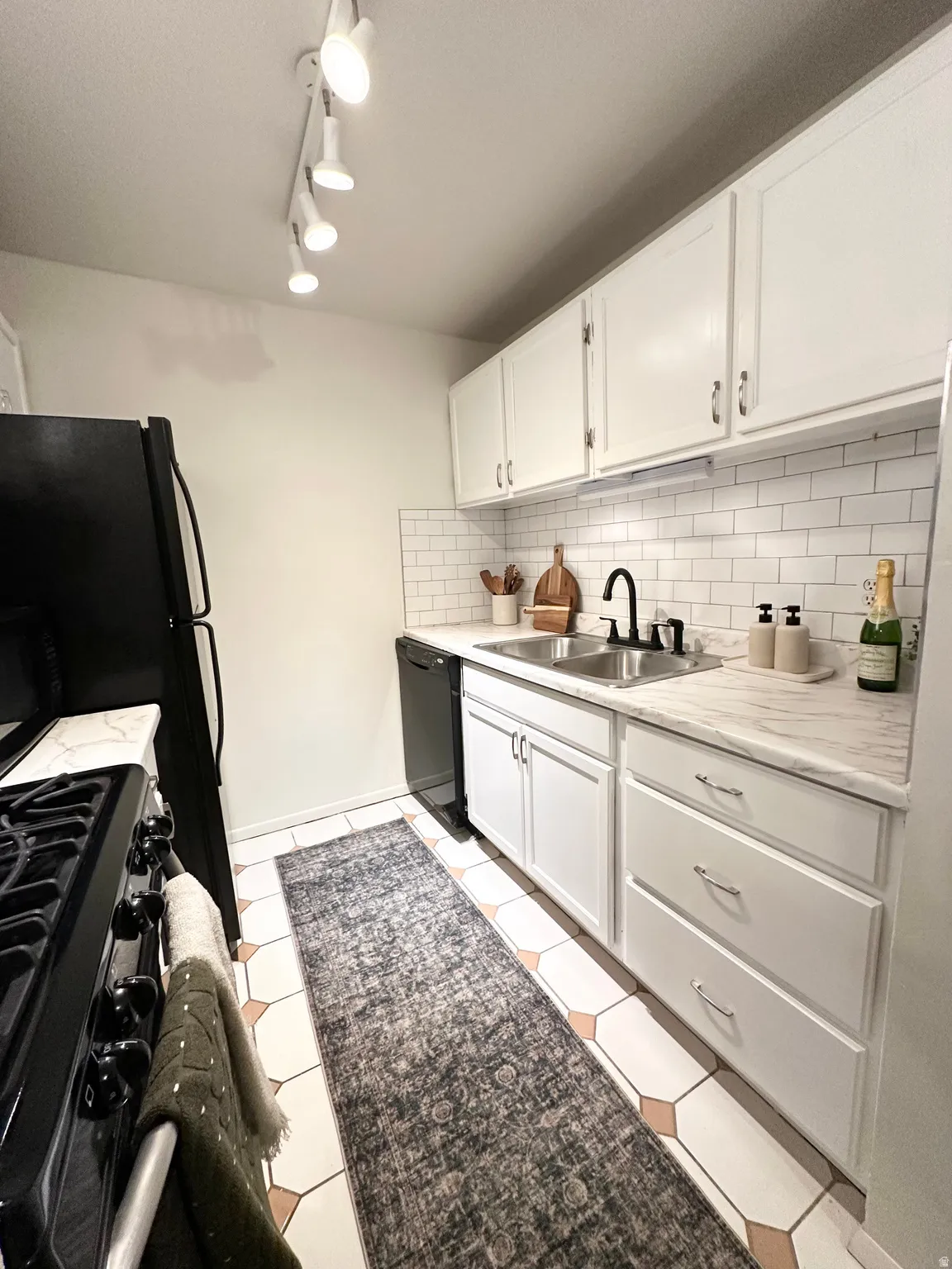 Kitchen featuring white cabinets, light countertops, black appliances, decorative backsplash, and light tile patterned floors