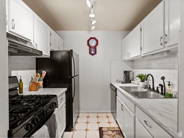 Kitchen with backsplash, black gas range, white cabinetry, under cabinet range hood, and light floors