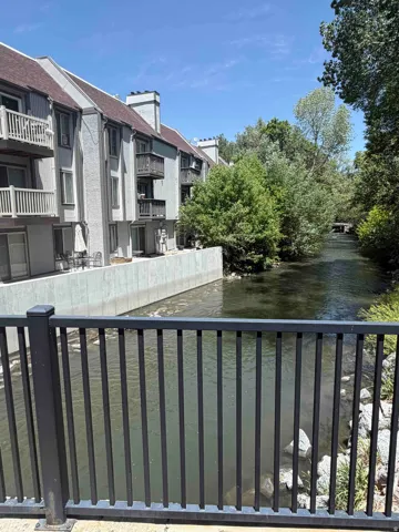 Riverfront property featuring multiple balconies, a river retaining wall, mature trees, and a black metal railing