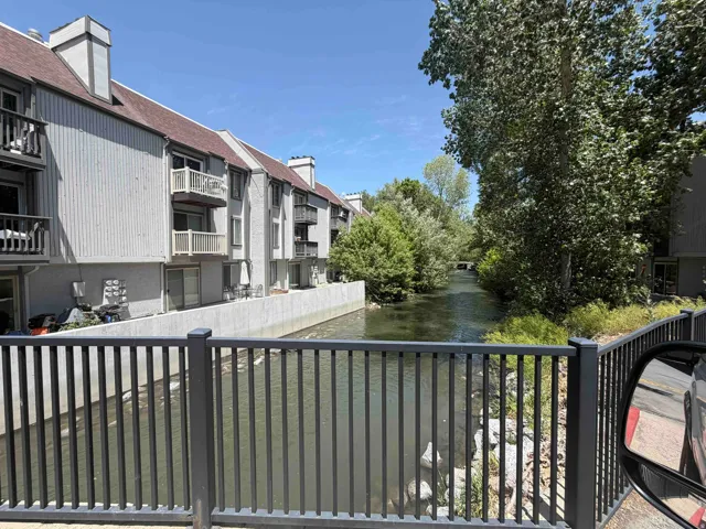 Waterfront multi-story building featuring individual balconies, private patios, and mature trees lining the waterway