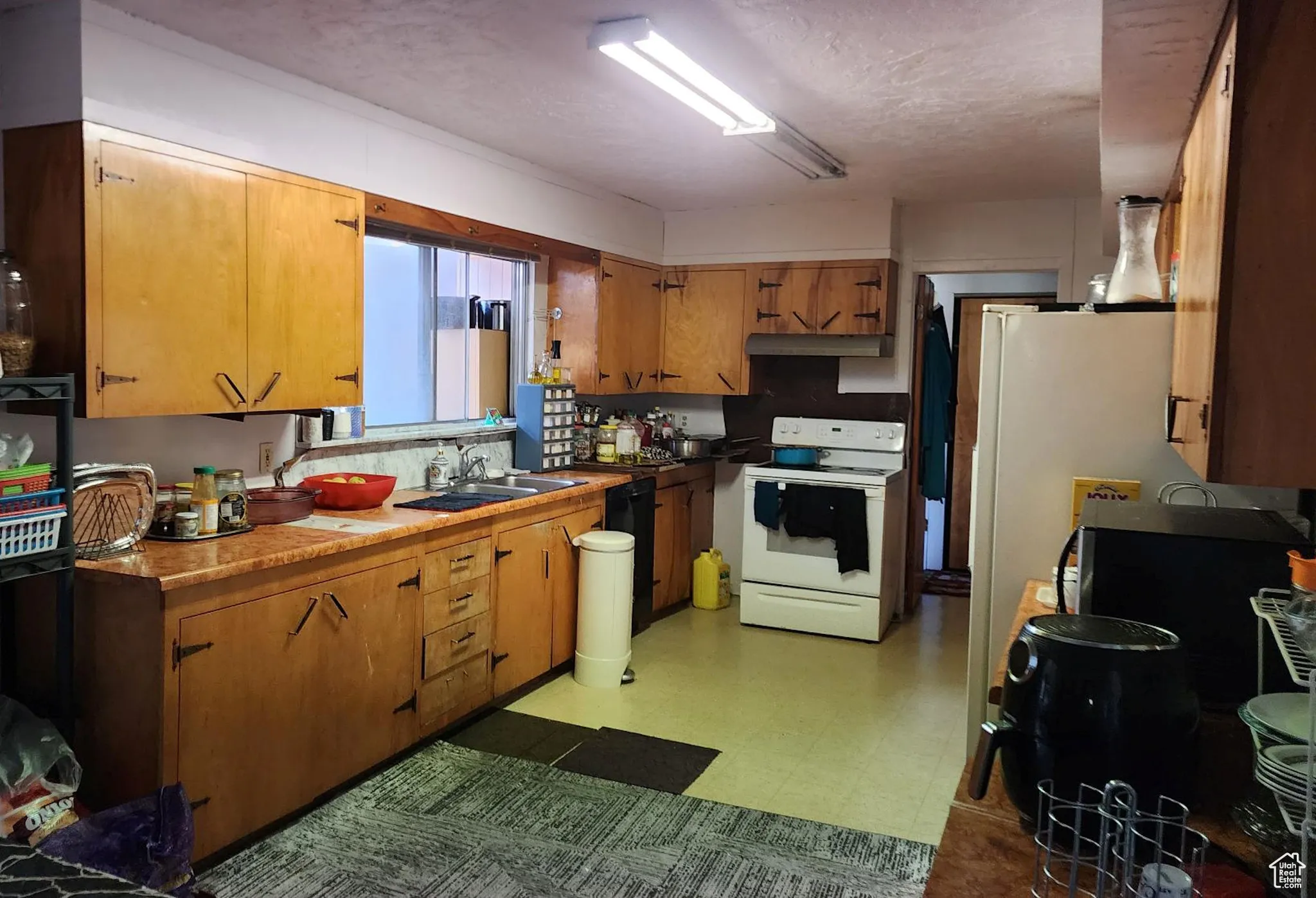 Kitchen with light flooring, electric range, a textured ceiling, fridge, and black dishwasher
