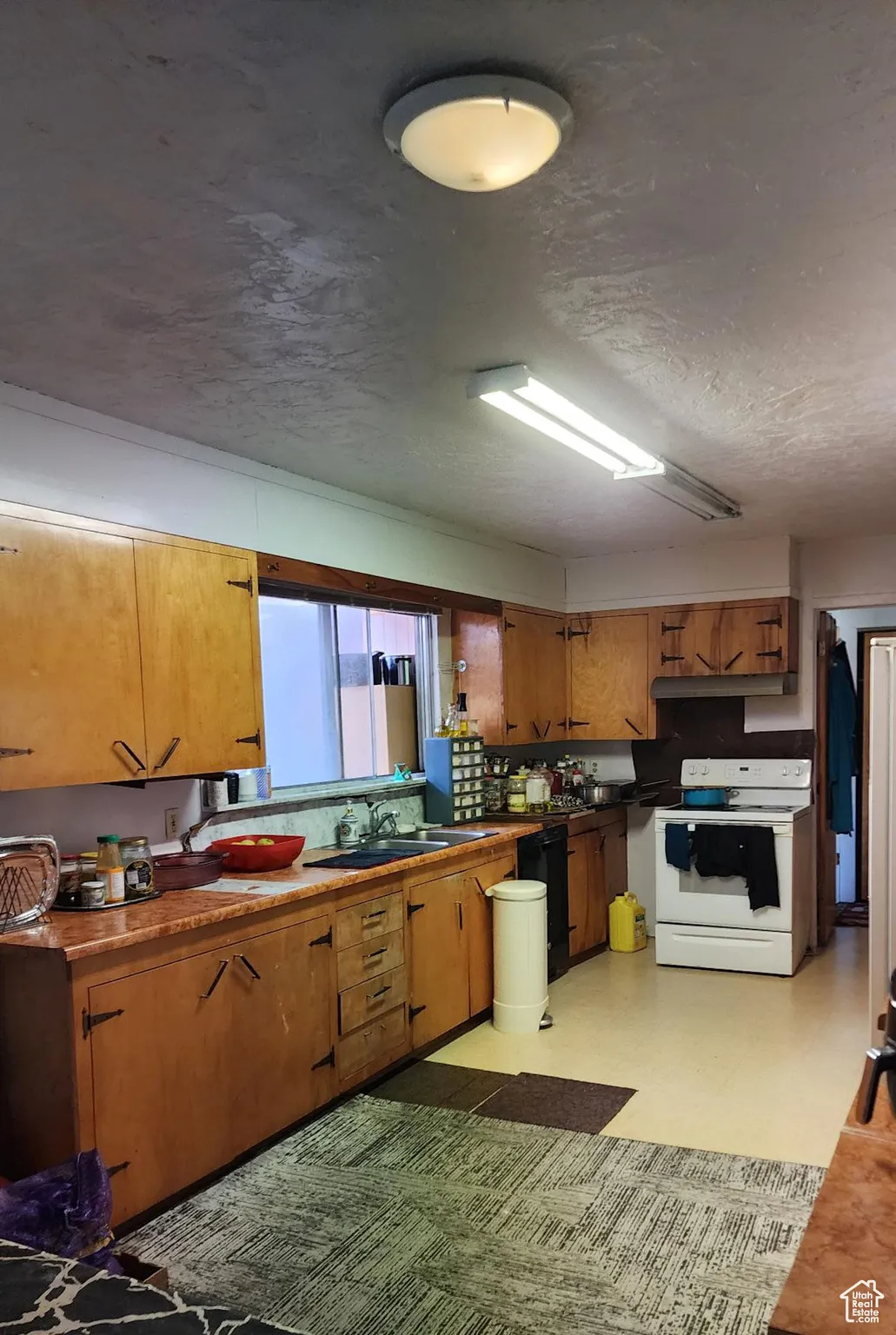 Kitchen with light floors, white range with electric cooktop, a textured ceiling, brown cabinetry, and dishwasher