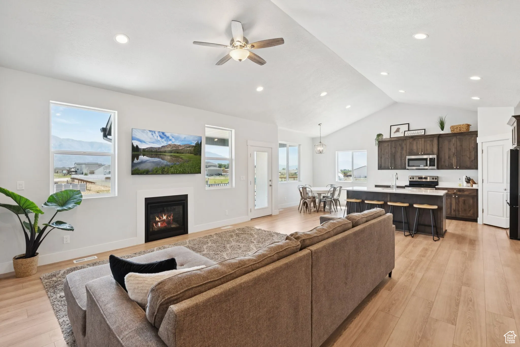 Living room featuring light wood finished floors, a glass covered fireplace, a ceiling fan, recessed lighting, and high vaulted ceiling