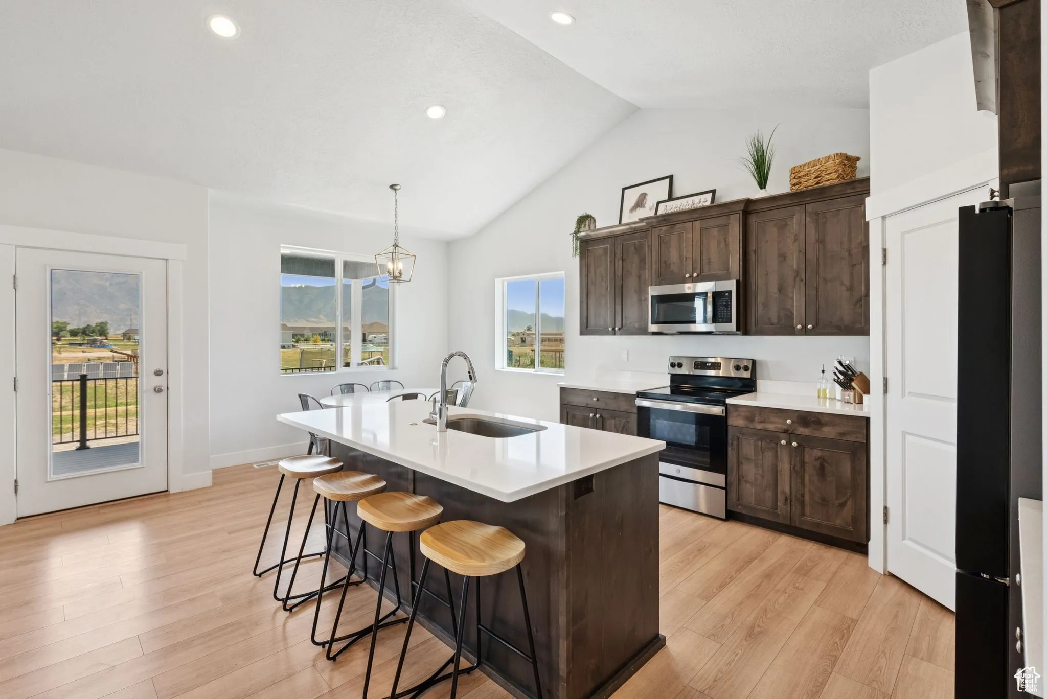 Kitchen with appliances with stainless steel finishes, a kitchen bar, dark brown cabinets, light wood-style floors, and light countertops