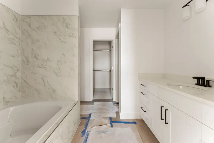 Full bathroom featuring vanity, a garden tub, a walk in closet, and light wood-type flooring