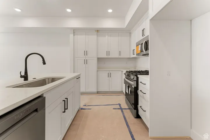 Kitchen with recessed lighting, white cabinets, stainless steel appliances, light stone countertops, and inlaid floor details