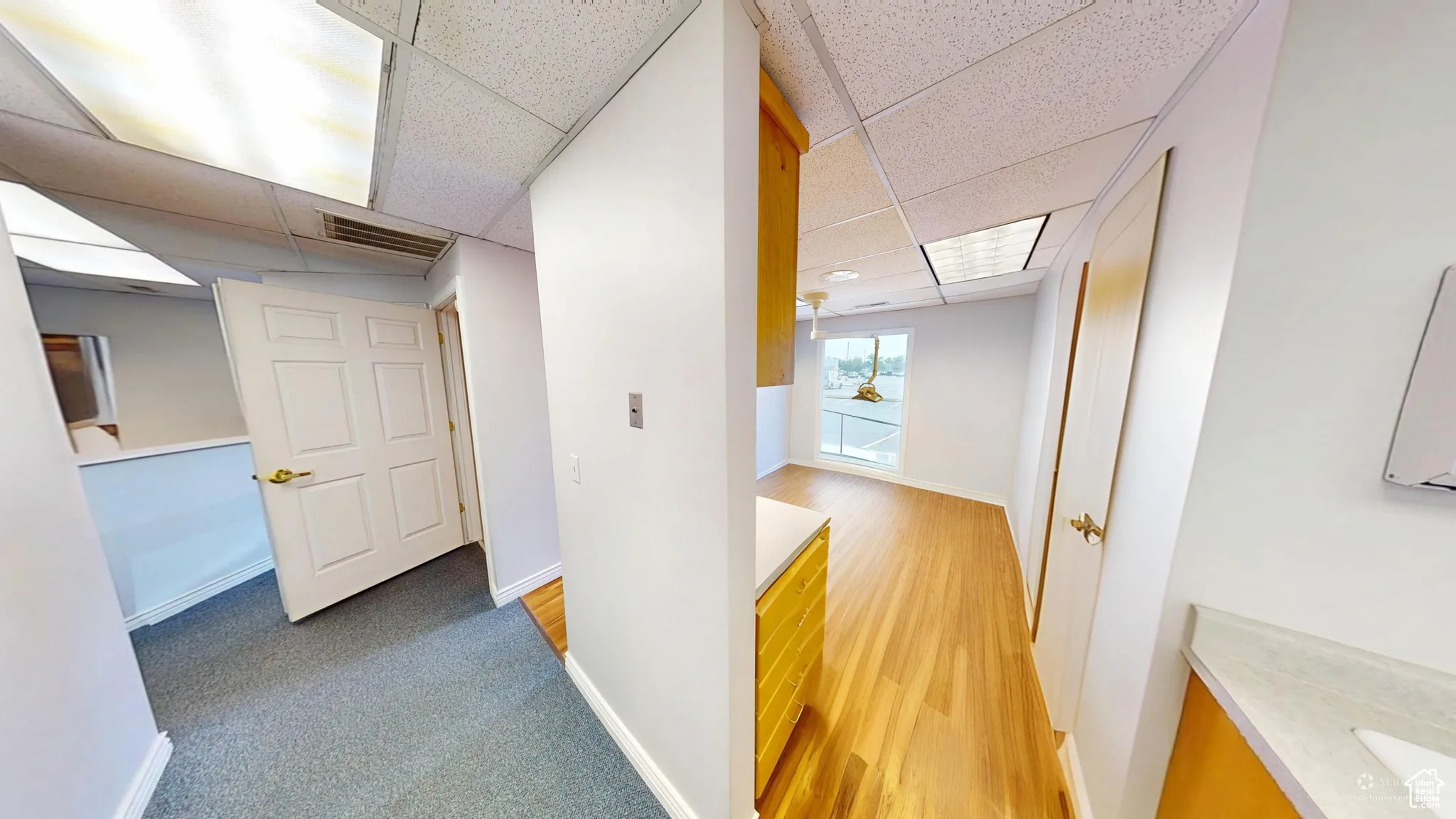 Hall featuring a paneled ceiling, light carpet, and light wood-style flooring