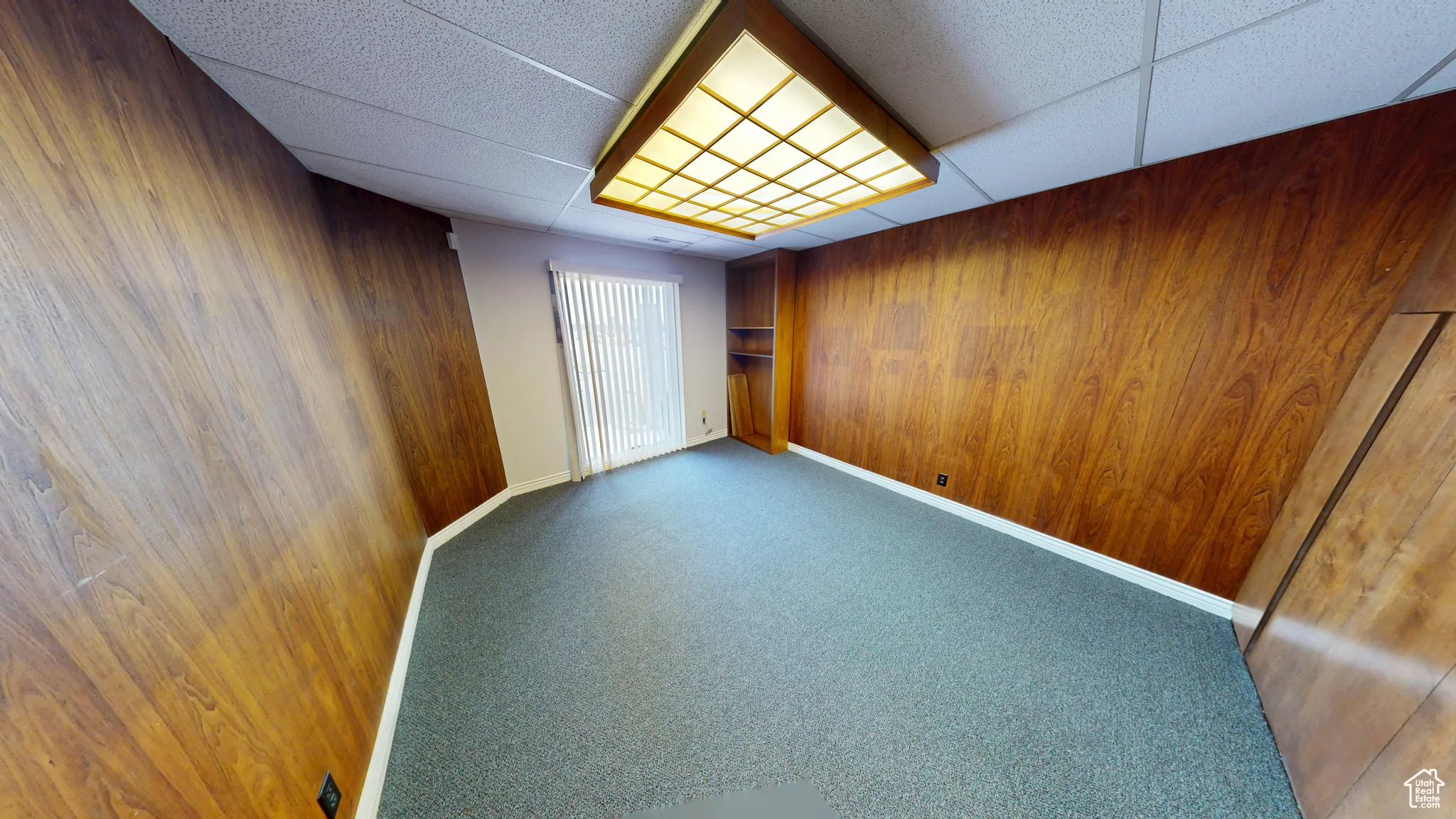 Unfurnished bedroom featuring wooden walls, carpet, a paneled ceiling, and a closet