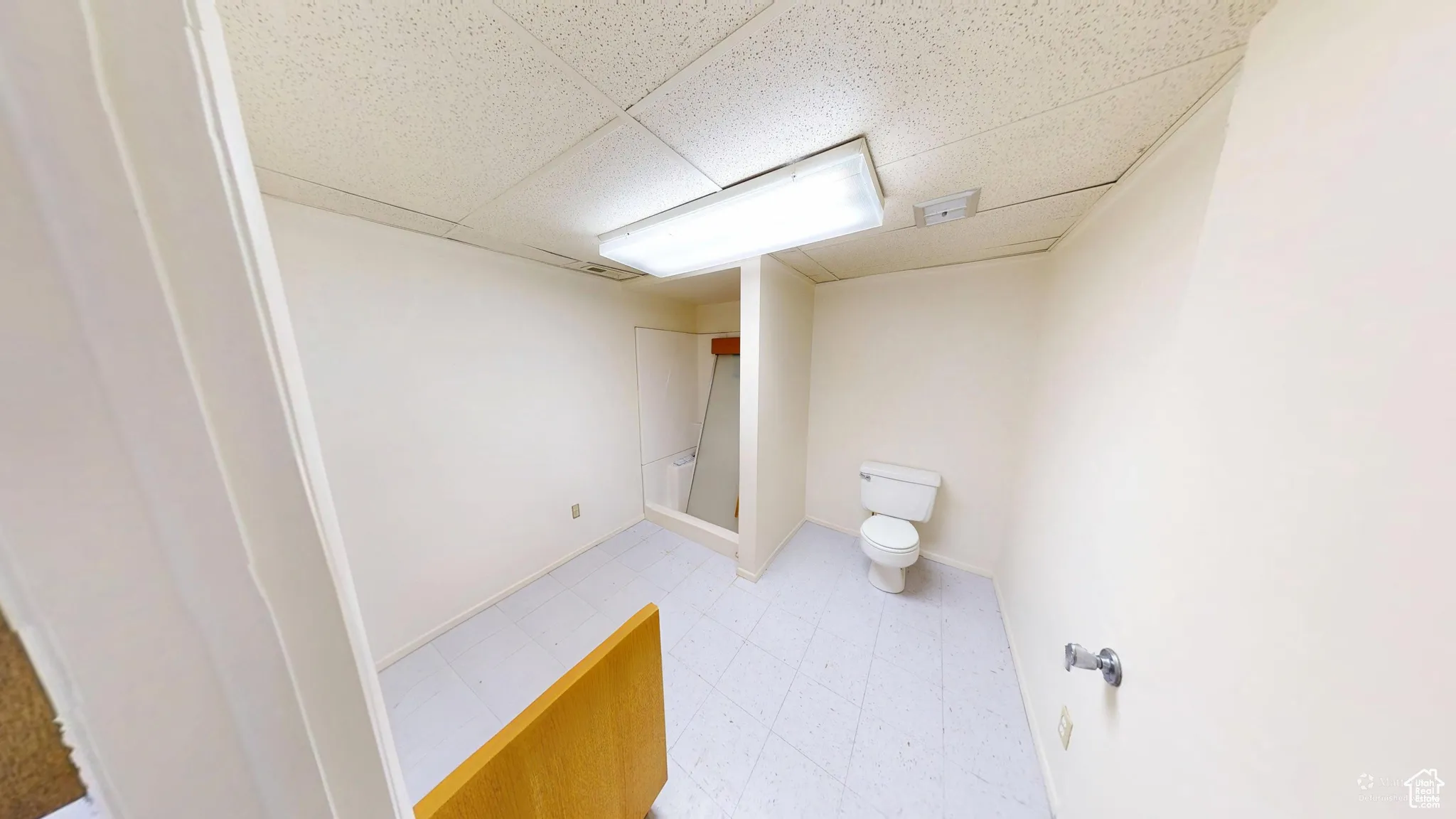 Bathroom featuring a drop ceiling, light flooring, and a stall shower
