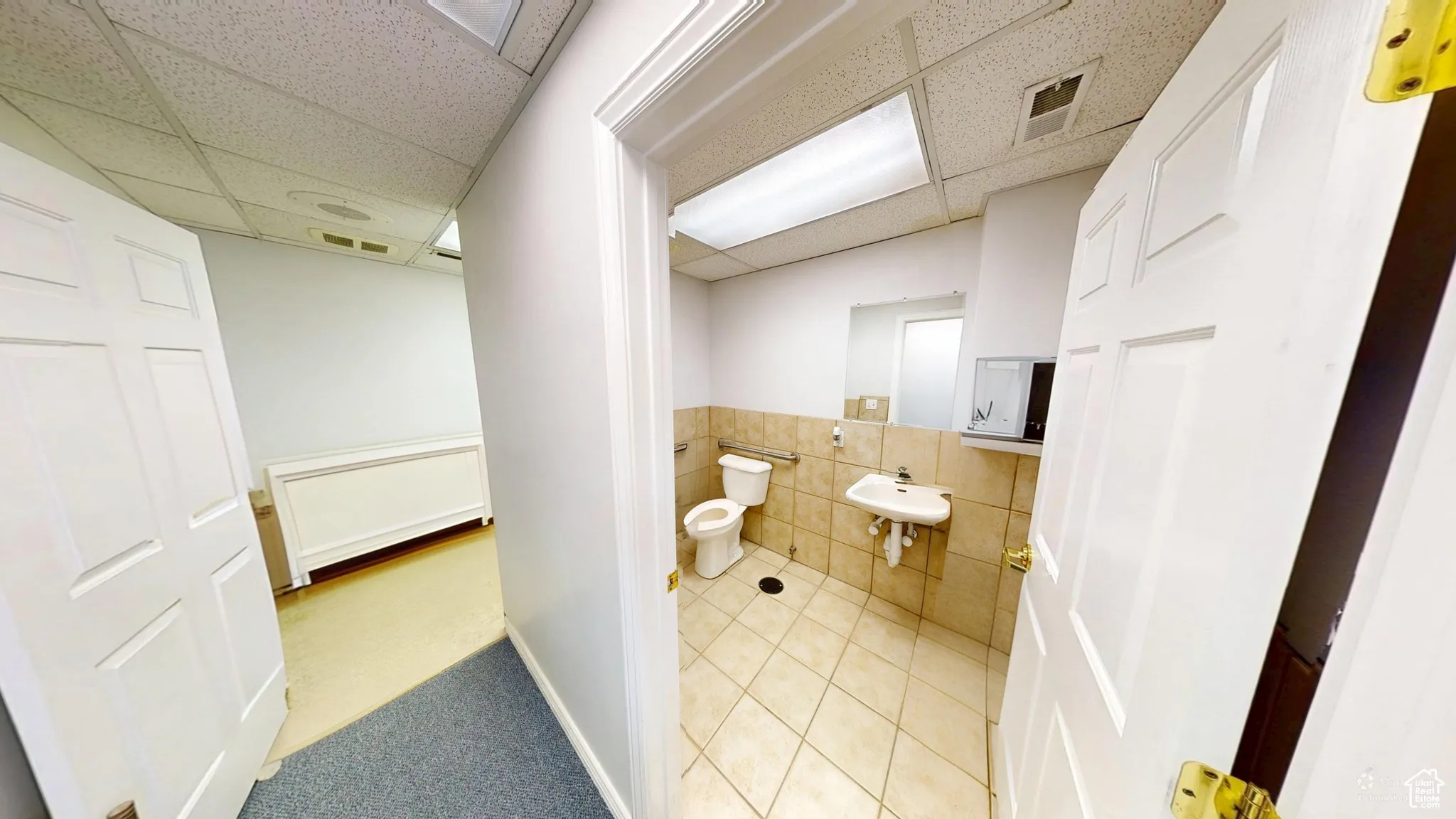 Half bath featuring light tile patterned flooring, a wainscoted wall, tile walls, and a paneled ceiling