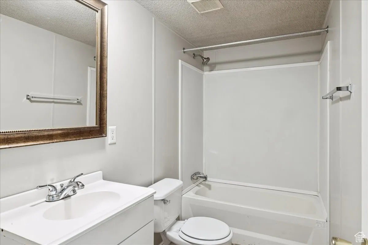 Full bath featuring a textured ceiling, vanity, and tub / shower combination