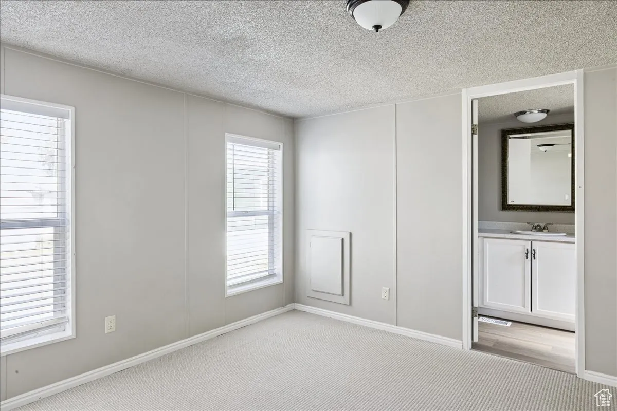 Unfurnished bedroom featuring light colored carpet, a textured ceiling, and ensuite bathroom