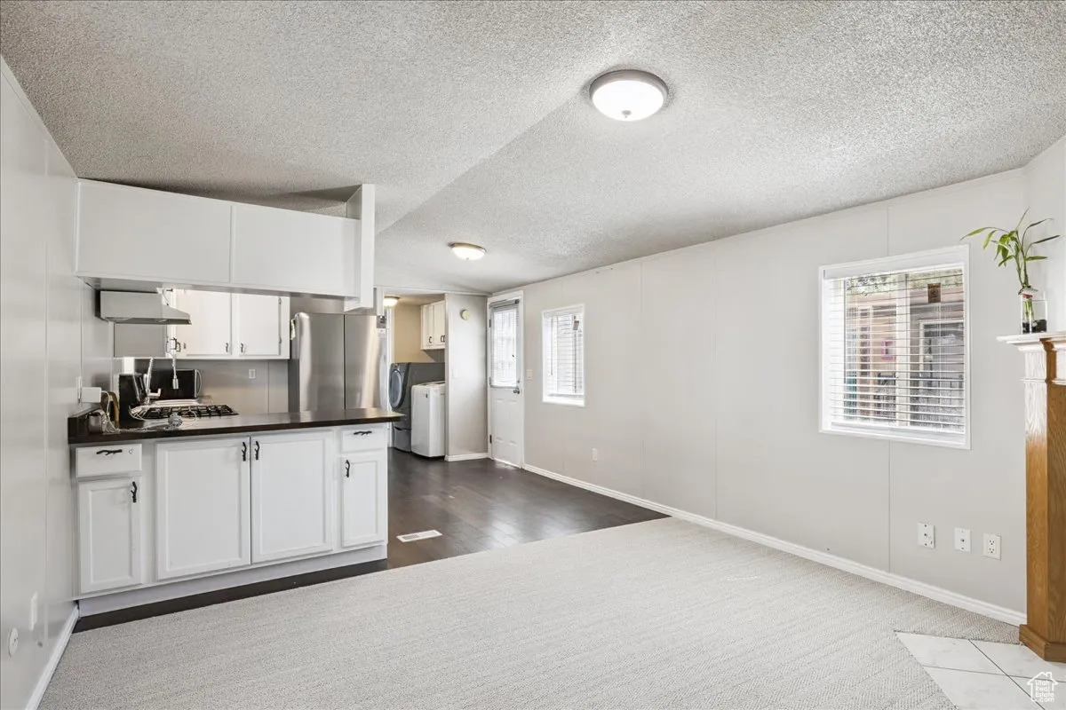 Kitchen featuring washer and dryer, dark countertops, freestanding refrigerator, a textured ceiling, and white cabinetry