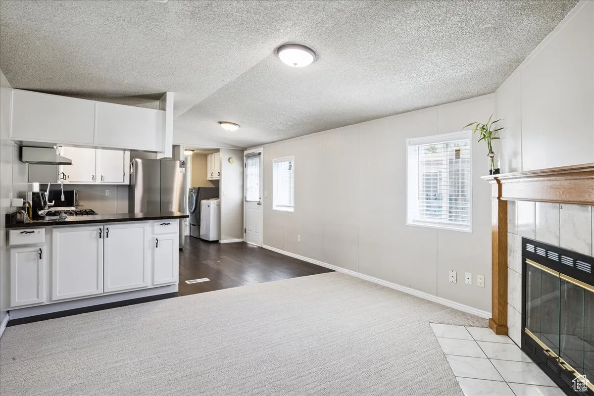 Kitchen with washing machine and clothes dryer, dark countertops, a fireplace, vaulted ceiling, and a textured ceiling