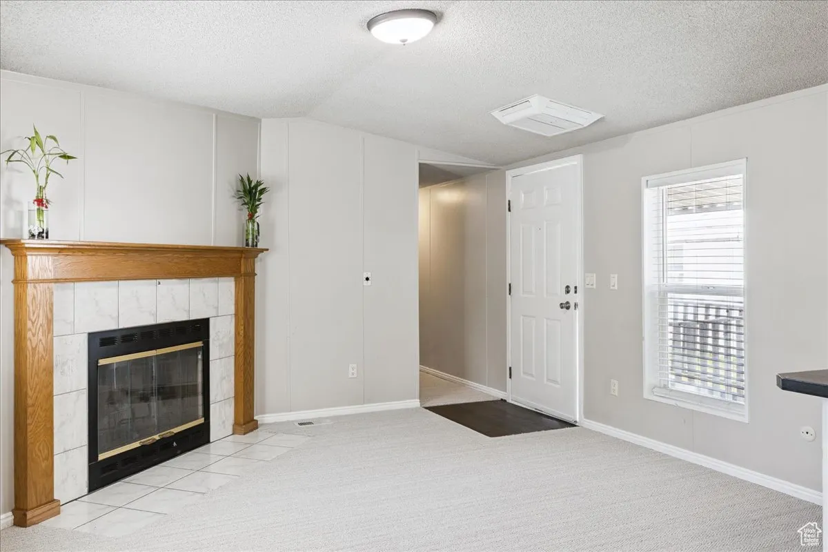 Unfurnished living room featuring a textured ceiling, carpet, and a tile fireplace