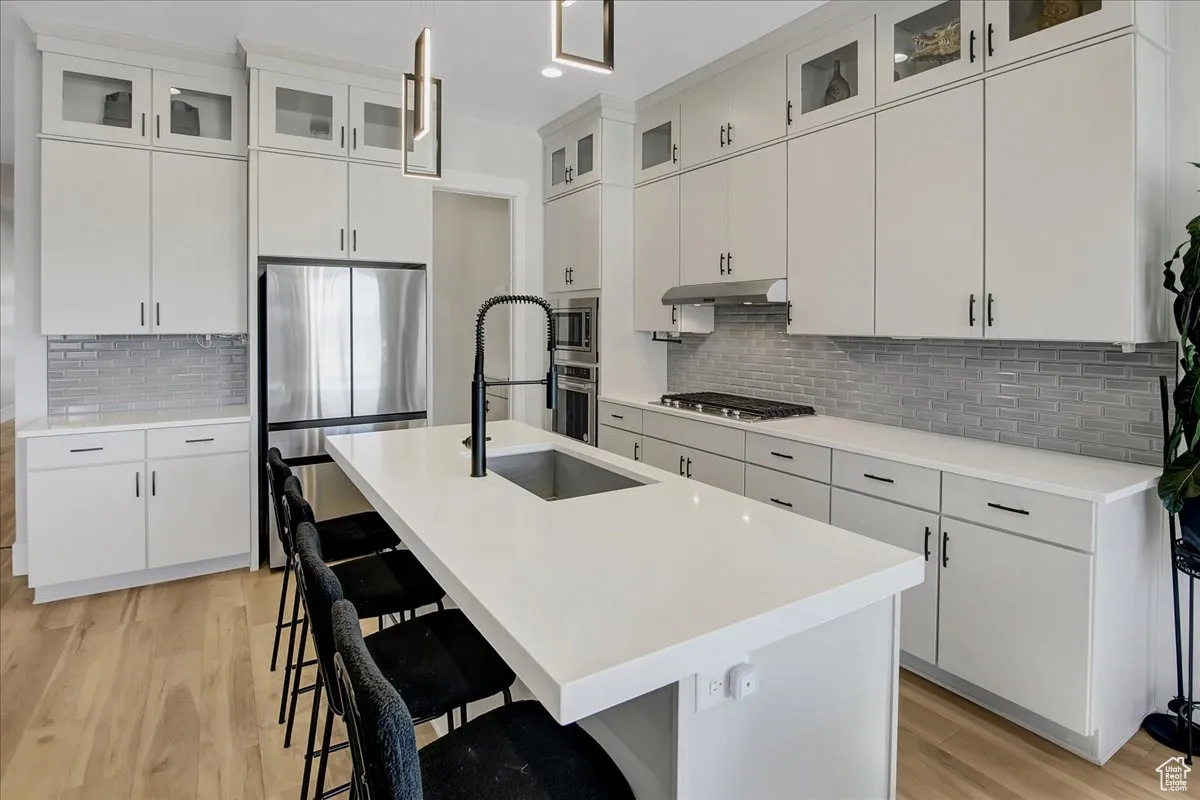 Kitchen featuring appliances with stainless steel finishes, light wood-type flooring, backsplash, a breakfast bar area, and recessed lighting