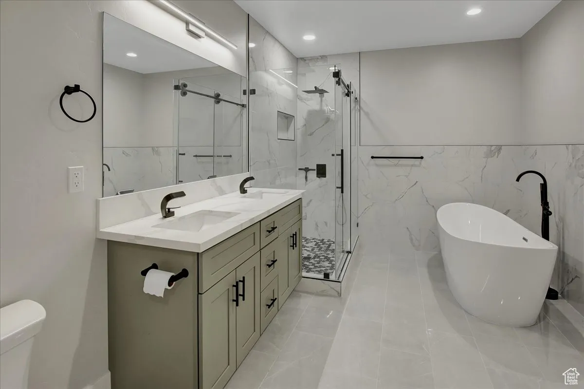 Bathroom featuring tile walls, a marble finish shower, a freestanding tub, double vanity, and a wainscoted wall