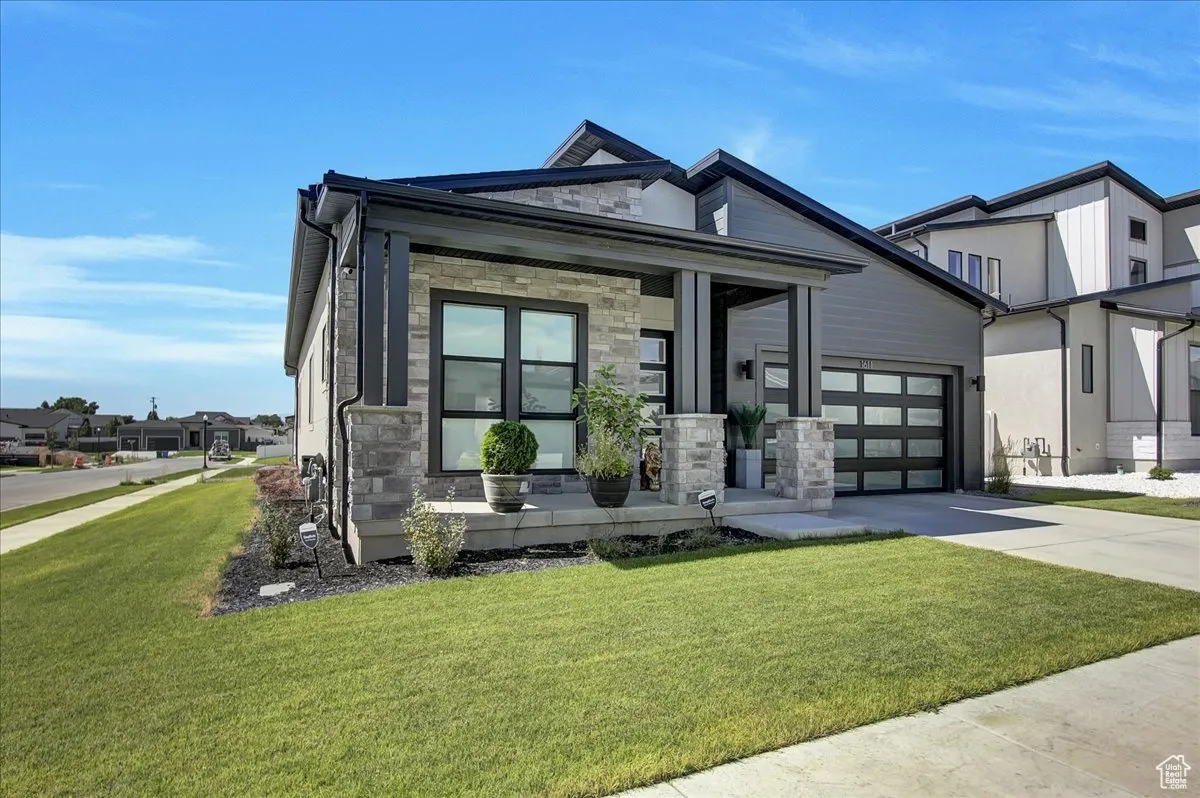 View of front of home featuring stone siding, concrete driveway, covered porch, a garage, and a front yard