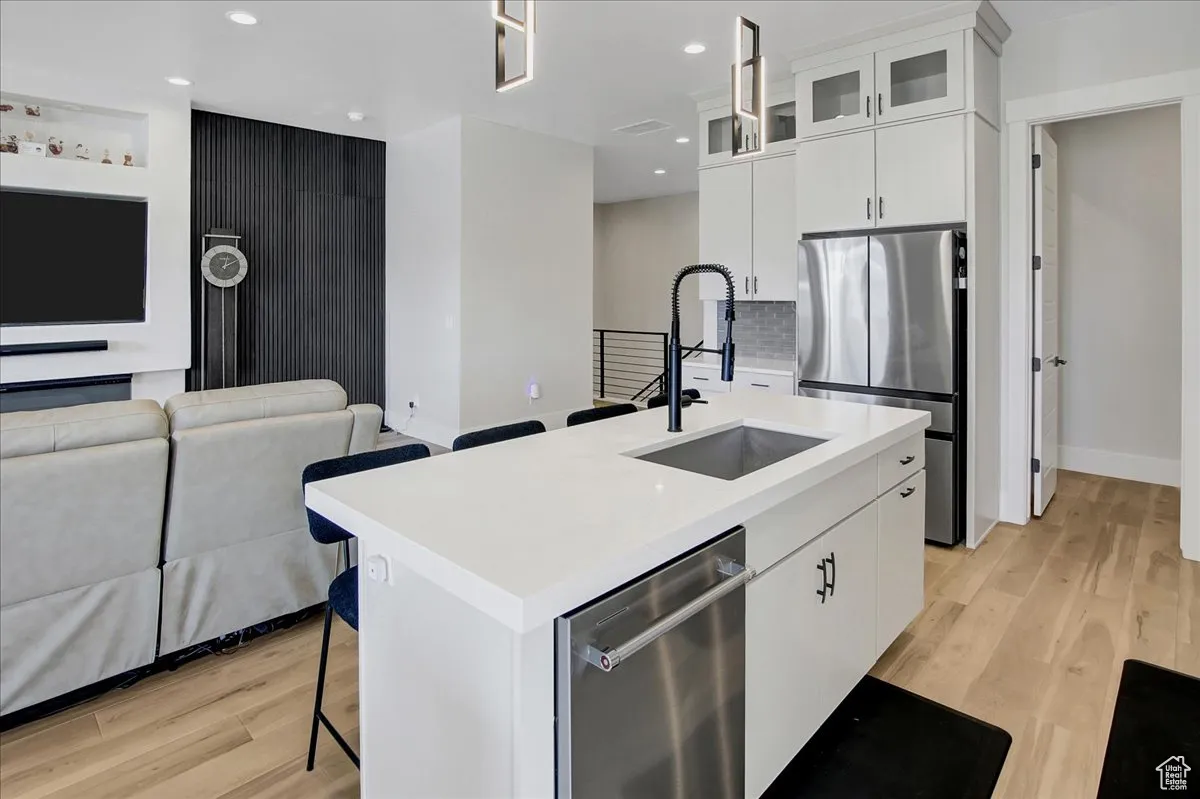 Kitchen with stainless steel appliances, light wood-type flooring, a kitchen island with sink, open floor plan, and recessed lighting