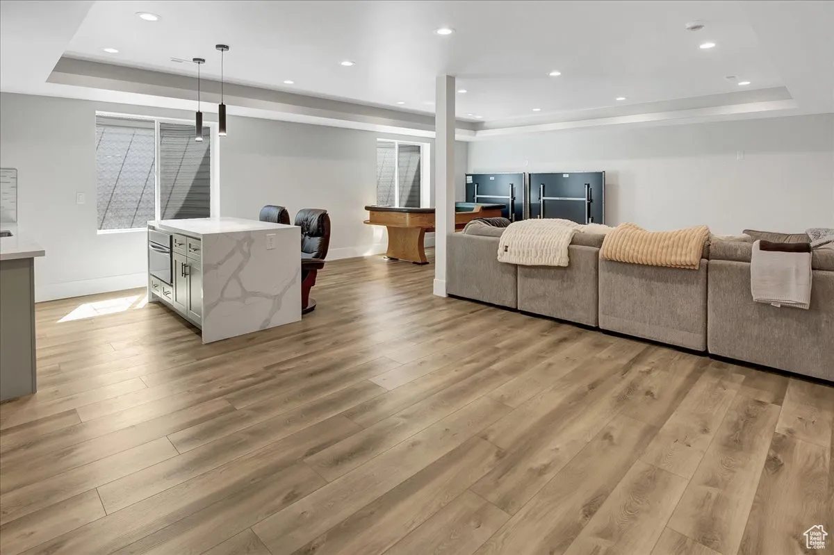 Living area with a tray ceiling, light wood finished floors, and recessed lighting