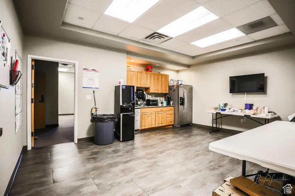 Kitchen featuring a drop ceiling, stainless steel refrigerator with ice dispenser, freestanding refrigerator, and light brown cabinetry